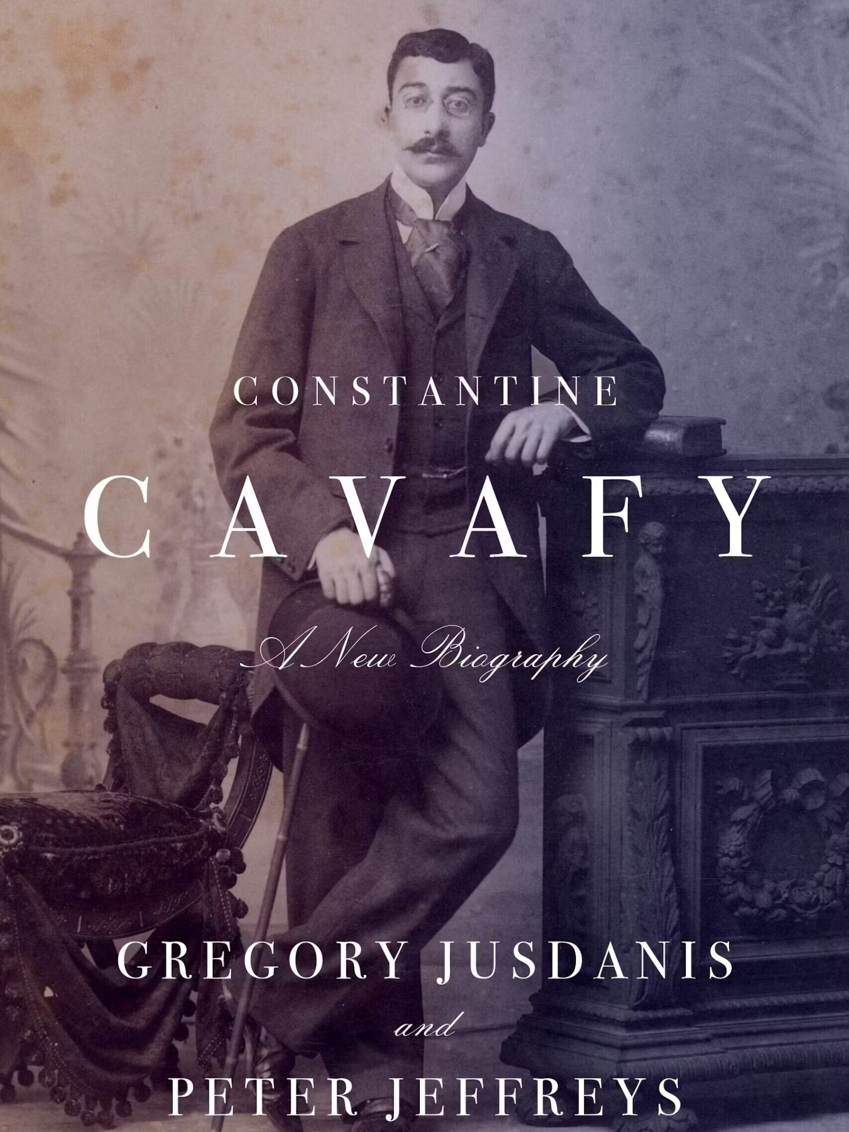 A sepia-toned book cover features a portrait of Constantine Cavafy, a mustached man in a suit, leaning on an ornate table. The title reads Constantine Cavafy: A New Biography by Gregory Jusdanis and Peter Jeffreys.