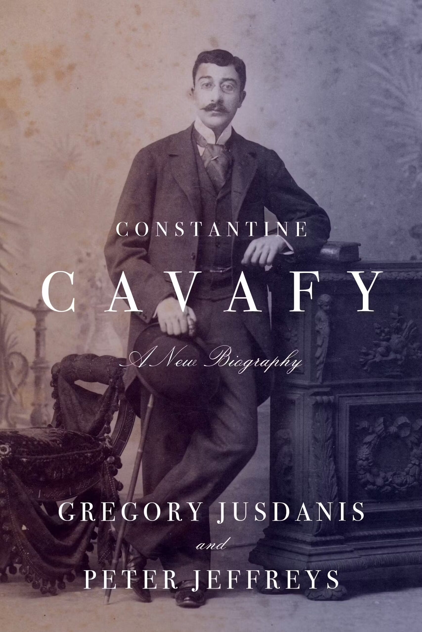 A sepia-toned book cover features a portrait of Constantine Cavafy, a mustached man in a suit, leaning on an ornate table. The title reads Constantine Cavafy: A New Biography by Gregory Jusdanis and Peter Jeffreys.